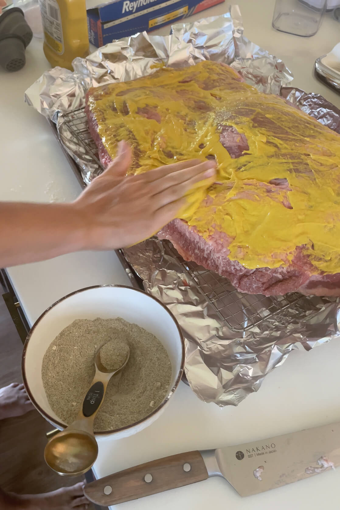 Covering a brisket with mustard before smoking.